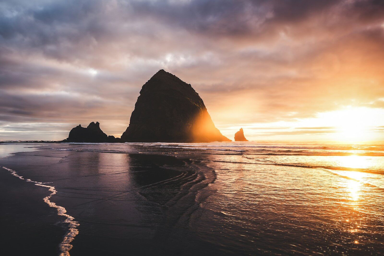 Dramatic sunset over a rocky coastline with wet sand.
